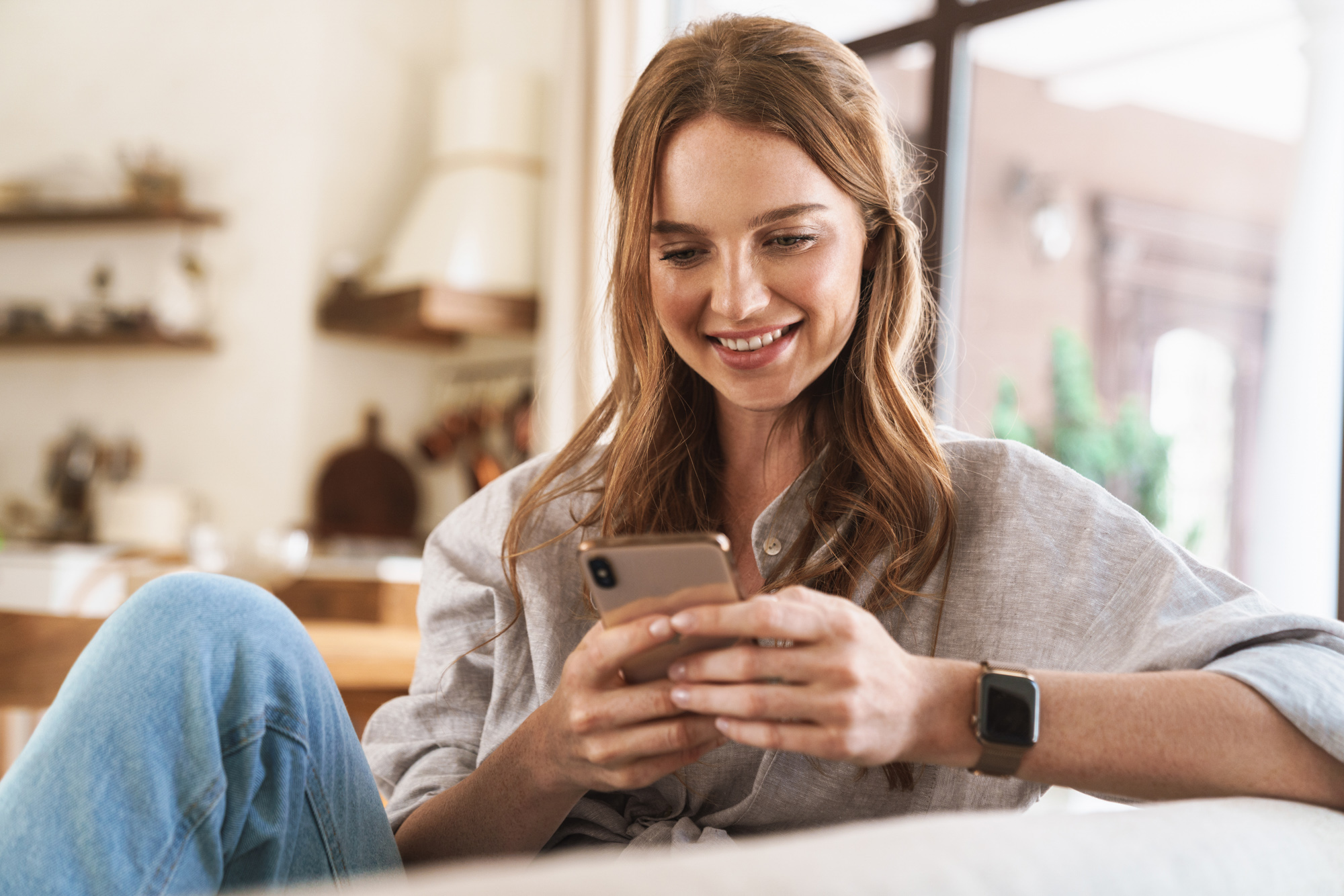 Happy woman sitting on the couch scheduling an appointment at Exhibit Medical Aesthetics for lash extensions near Chatham, NJ.